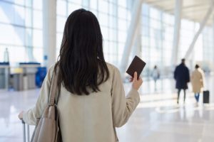空港の明るい出国ゲートと、手元のパスポート（顔なし）